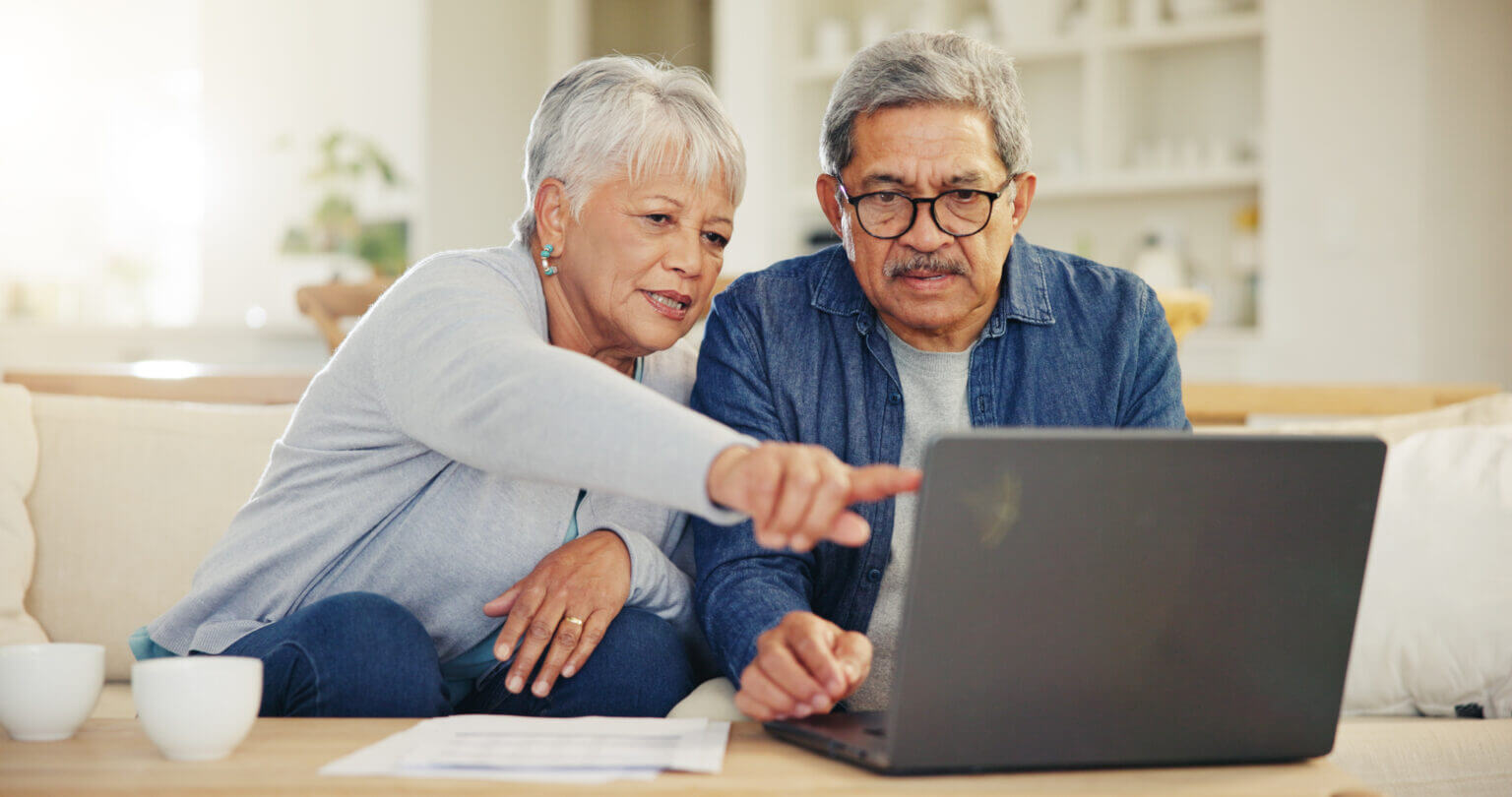 Senior, couple and planning on laptop in living room with document for finances, investment or retirement. Elderly man, woman and pointing by technology for online banking, account balance or savings Senior, couple and pointing on laptop in living room with document for financial planning, investment or retirement. Elderly man, woman and technology for online banking, account balance or savings